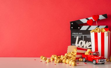 Sevgililer Günü drama galası. El çırpma tahtası, minyatür teslimat arabası çizgili patlamış mısır kutuları ve kırmızı duvarda kalp dekoru olan bir masanın yan görüntüsü. Sevgi dolu atmosferi kucakla.