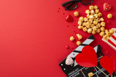 Love Reel Unpeiled: Bir klaket tahtası, 3D gözlükler, dağınık patlamış mısır, çikolata ve kırmızı bir yüzey üzerinde kalp şeklinde dekorasyonlar yakalıyor ve romantik bir film galasını duyuruyor.