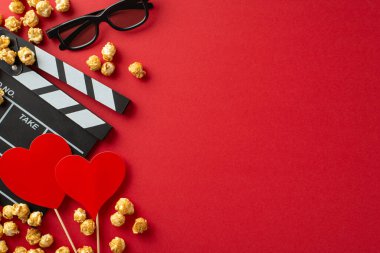 Romantik Film Buluşma Ayarları: alkış tahtası, 3D gözlükler, lezzetli patlamış mısır ve büyüleyici kırmızı arka planda kalp şeklinde dekorasyon.