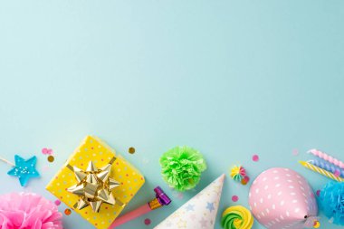 Dinamik yıldönümü teması. Üst manzara dekoratif aksesuarlar, lolipoplar, hediye, doğum günü şapkaları, gürültü çıkarıcı, mumlar, konfeti, pastel mavi arka planda çiçekler, metin için yer