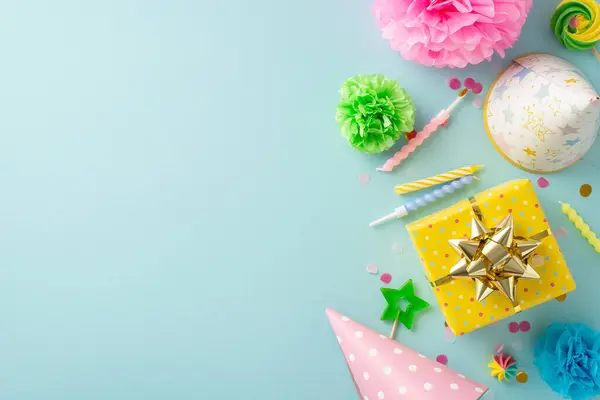 Vibrant party theme inspiration. Overhead shot of a celebratory setup with gift, hats, candles, flowers, confetti, and more on a cheerful pastel blue backdrop. Ideal for text or ads