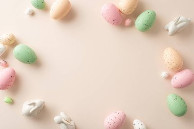 Paskalya cazibesi aranjmanı bu üst görünümde sergileniyor. Klasik bıldırcın yumurtaları, pastel bej bir tuval üzerinde tatlı seramik tavşanlar, metin veya promosyon için çerçeveli.