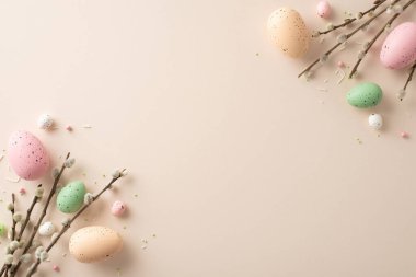 Easter elegance captured in single frame. Top view vibrant eggs, graceful pussy-willow twigs, sprinkles create picturesque scene on pastel beige background. Ideal for your custom text or advertisement
