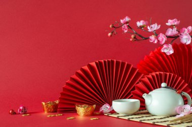Çin Yeni Yıl yan görünüş kompozisyonu: Feng shui öğeleri, çaydanlık, çay fincanı, sakura çiçekleri ve hayranlar kırmızı arka planda sanatsal olarak bol miktarda metin veya reklam alanı ile yerleştirilmiştir.