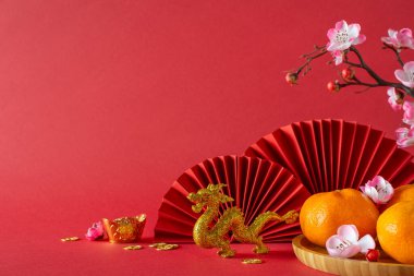 Geleneksel Yeni Yıl tablosu: kenar görünümü feng shui öğeleri, ejderha süsü, mandalinalı tabak, sakura, fanlar kırmızı arka plana sanatsal olarak yerleştirilmiş, metin veya promosyonlar için mükemmel tuval