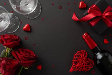 Doğum günü partisi sofistike. Üstten çekimde çeşitli çikolatalar, şarap şişesi, gözlük, hediye kutusu, canlı güller, şık siyah yüzey üzerinde kutlama konfetisi, reklam alanı...