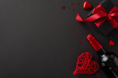 Özel Sevgililer Günü Zarafeti: Görkemli bir yemek takımının entellektüelliğini bir şarap şişesi, kalp şeklinde bir çikolata, bir hediye kutusu ve rafine siyah bir arka planda konfeti ile yakalamak.