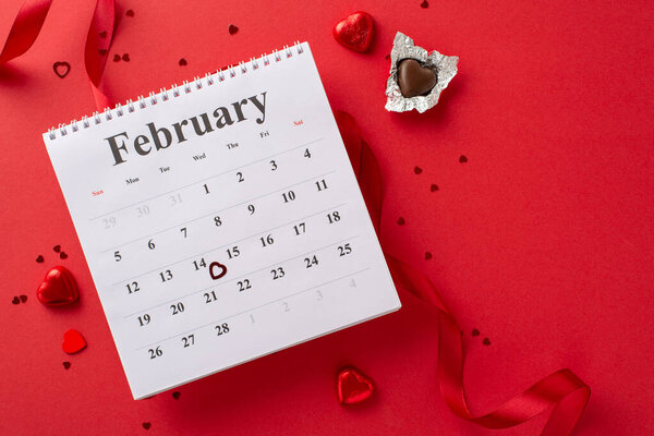 Romantic preparations: top view February calendar, chocolates, silk ribbon, and confetti laid out on a red canvas. Add your personal touch or promotional content