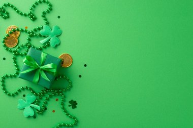 Yeşil temalı kutlama: Üstten çekimde hediye kutusu, şanslı altın sikkeler, folyo, konfeti ve boncuk kolye yer alan yeşil bir zemin üzerinde metin için boşluk