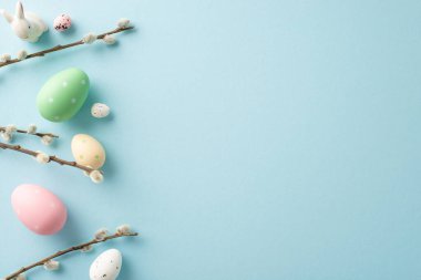 İlkbahar büyüsü yakalandı: canlı yumurtaların üst görüntüsü, pastel mavi bir arka planda şirin bir tavşan. Metninizle kişiselleştirin