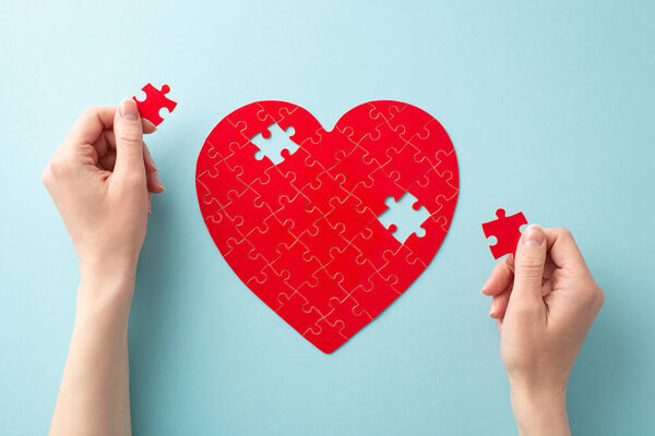 First person top view photo of female hands forming a heart puzzle with jigsaw pieces on pastel blue background for World Blood Donor Day