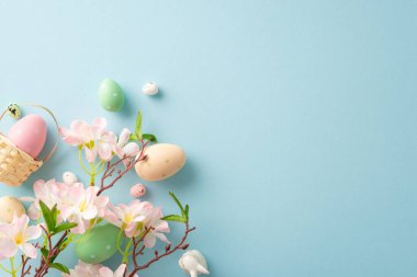 İlkbaharda yakalanan neşe: üst manzara minyatür sepet, canlı yumurtalar, tatlı bir tavşan, pastel mavi arka planda elma çiçekleri. İletiniz için özelleştirilebilir boşluk