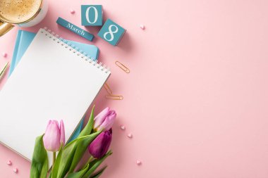 İş yeri Kutlaması: 8 Mart 'ı vurgulayan küp takvimi ile süslenmiş bir masanın üst görünümü. Taze kahve, not defterleri, kalem, klipler ve mesajınız için pembe arka planda yer alan laleler.