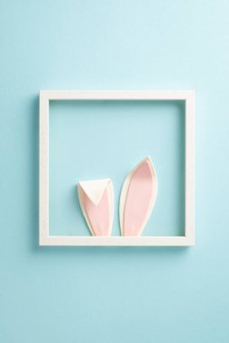 Neşeli Paskalya mutluluk sahnesi. Bir fotoğraf çerçevesinde saklanan büyüleyici bir Paskalya tavşanının dikey çekimi. Kulakları mavi bir arka planda neşeyle fırlıyor.