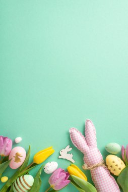 Paskalya ruhunu yakala! Canlı yumurtaların, şirin tavşan oyuncakların ve lalelerin dikey görüntüsü. Turkuaz arka plan neşeli bir dokunuş ekliyor, Paskalya kutlamalarınız için yer bırakarak.