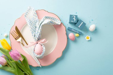 Bunny Ears Brunch: Temalı masa ortamının en iyi görüntü fotoğrafıyla Paskalya terfilerinizi yükseltin. Tabak, tavşan kulaklı peçete, 31 Mart küp takvim, laleler, serpinti, pastel mavi arka planda yumurtalar