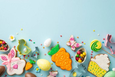 Paskalya temalı şekerleme sahnesi. Kurabiye keskisi gibi temel şeyleri pişiren bir masanın en üst görüntüsü. Lezzetli zencefilli ekmekler, çikolatalı yumurtalar, açık mavi bir yüzey üzerinde açık mavi lolipoplar.