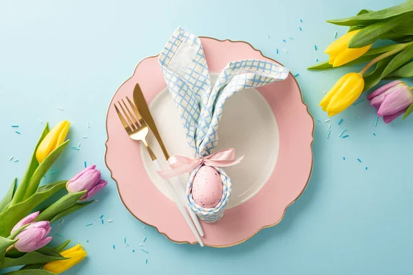 Eggstraordinary Dining: Top view of a delightful Easter table setup featuring a plate, bunny ear napkin with egg, cutlery, bright tulips, sugar sprinkles. Pastel blue background, perfect for text