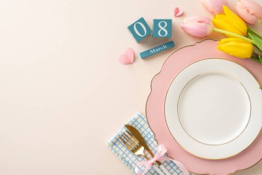 Kadın Günü için ilham kaynağı: rafine bir tabağın, peçetenin, çatal bıçak takımının, bir demet lalenin, tarih bloklarının ve kalplerin yukarıdan aşağı görünümü mesajınız için yumuşak bej bir tuval üzerinde.