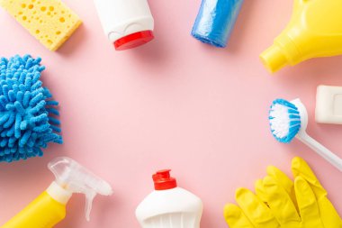 Temizlik gereksinimlerinin en üst görünümü: dezenfektan spreyi, sabunlar, eldivenler, toz bezi ve sünger, mesajınız için geniş bir alana sahip soluk pembe arkaplan üzerine kuruludur.