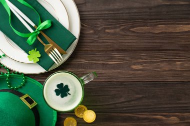 St. Patrick 'in şerefine kadeh kaldıralım: Tabağın üst görüntüsü, peçeteye sarılmış çatal bıçak, bir bardak bira, leprikon şapkası, altın sikkeler, trefolyolar, ahşap masa örtüsü. Şenlik anonsların için mükemmel.