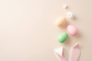 Neşeli bir tatil aşığı sahnesi. Gizli tavşan kulakları üzerinde süzülen canlı yumurtaların yüksek açılı üst görünümü sessiz bir bej arka plan, mesaj veya reklam için boş bir alan ile