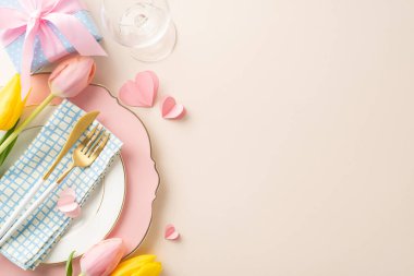 Kadınlar Günü kutlaması için masa hazırlıyorum. Zarif tabaklar, peçeteler, çatal bıçaklar, şarap kadehleri, büyüleyici laleler, hediye ve kalpler içeren bej renkli bir yüzey.