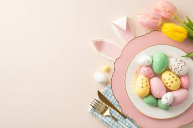 Paskalya ziyafeti masası konsepti. Tepede canlı yumurtalar, tavşan kulakları, çatal bıçak ve zarif lallar var. Yumuşak bej arka planda, mesaj için yer bırakıyorlar.