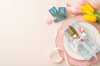 Zarif Kadınlar Günü masa örtüsü düzenleme, lüks bir tabak, gümüş takımlar, canlı laleler, hurma küpleri, kurdele ve kalpler, hepsi yumuşak bej bir zemin üzerine kuruludur.