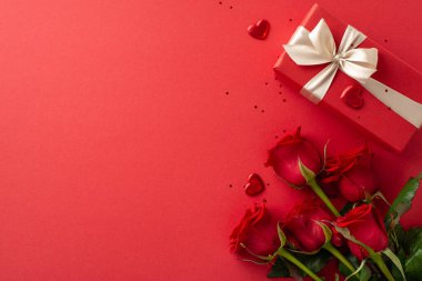 Zarif bayanın hediye sahnesi: üst manzara bol güller, şık bir hediye, kalpler ve pırıltı kırmızı bir yüzey üzerinde, metin veya tanıtım için tasarlanmış