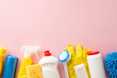 Temel temizlik seti özenle düzenlenmiş: üst görünüm sıvı temizleyiciler, toz bezi, koruyucu eldivenler, çöp torbaları ve sünger, metin veya reklamlar için alan minimalist pembe arka plan
