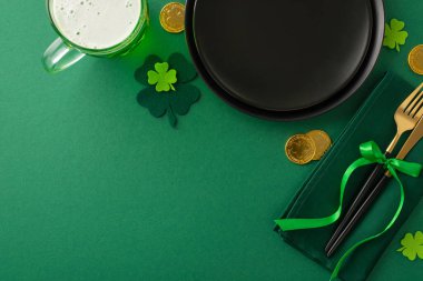 St. Paddy 's Day bar sahnesi yukarıdan çekildi: siyah tabak, çatal bıçaklı peçete, bira dolu bardak, altın sikkeler, folyo, canlı yeşil bir arka planda düzenlenmiş