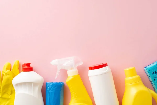 Ideal for home cleaning, this overhead shot features cleaning spray, dish soap, washing gel, gloves, garbage bags and sponge, neatly arranged on a soft pink backdrop with space for text