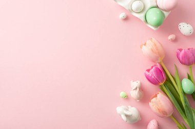 Paskalya ruhunu bu hoş sahne ile kucaklayın: üst görünüm düz bir kap canlı yumurta, garip tavşanlar ve soluk pembe yüzey üzerinde kokulu laleler, metin veya promosyonlar için ideal