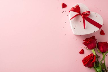 İdeal bayanın kutlama kurgusu. Zengin gül düzenlemesi, şık kalp şeklinde bir hediye, yumuşak pembe bir yüzeyde parıltı, mesajınız veya terfiniz için yer bırakarak.
