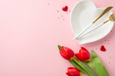 Mükemmel 8 Mart akşam planı. Yemek takımının üst görüntüsü, kalp şeklinde yemek takımı, zarif çatal bıçak takımı, sim, kalp aksanları, canlı laleler, yumuşak pembe yüzey, mesajınız ya da promosyonunuz için yer bırakın.