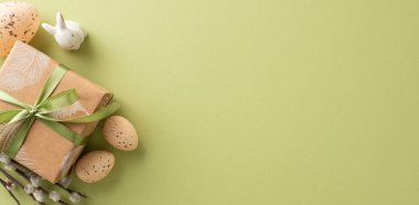 Folk Easter setting concept. Top view photograph of handmade gift parcel, rabbit, naturally decorated quail eggs, pussy willow cuttings, displayed on forest green mat with blank section for wording