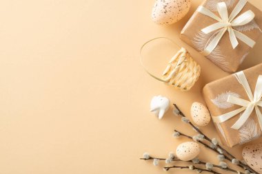 Enchanting Easter arrangement design. View from top capturing crafty gifts, miniature rabbit statuette, quail eggs, petite basket, lush pussy willow, arrayed on beige canvas with blank space for ad