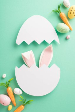 Paskalya sihirli tasarımı. Çatlak bir yumurtadan çıkan sevimli tavşan kulaklarının dikey görüntüsü, boyanmış yumurtalar, havuç gibi havuçlar, gök mavisi arka planda, mesaj veya reklamlar için boş bir alan.