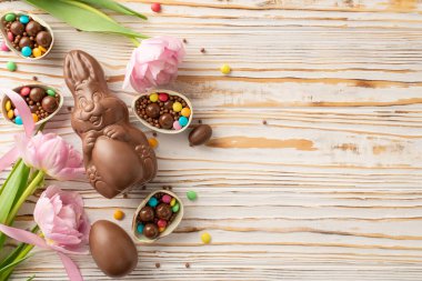 Tepeden bakıldığında büyüleyici Paskalya çeşitleri, çeşitli şekerlemelerle paketlenmiş çatlak çikolata yumurtaları, çikolata tavşanı, serpiştirmeler ve ahşap tabana serilmiş canlı laleler, artı metin için bir alan.