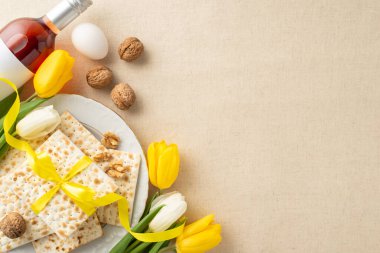 Hamursuz Bayramı sofrası ilham kaynağı: Kurdele, şarap, ceviz, yumurta ve sarı lalelerle çevrili matzo üst görünüm fotoğrafı, pastel bej keten masa örtüsü üzerinde düzenlenmiş, mesajlaşma alanı ile