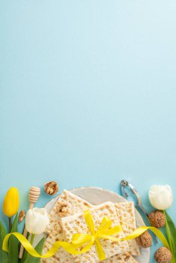 Sofistike Hamursuz Bayramı teması: üst görünüm dikey fotoğraf gösterimi matzası kurdele, fındık, yumurta, bal kırıcı, fındık kıracağı ve yumuşak mavi arka planda laleler, mesaj için boşluk