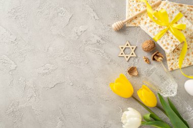 Kurdeleli matza, cam, ceviz, yumurta, bal kaplamalı ve laleli şık rengi Pesach seti, minimalist gri beton arka planda, metin tutucu ile dizilmiş.
