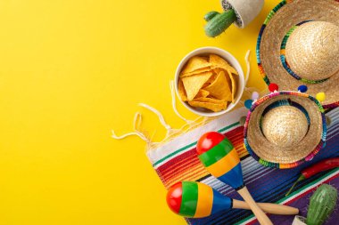 Cinco de Mayo aranjmanı. Geleneksel aksesuarların genel perspektifi: küçük boy sombreros, pitoresk marakas, kaktüs bitkisi, renkli serape, nachos dolu kase, sarı arka planda.