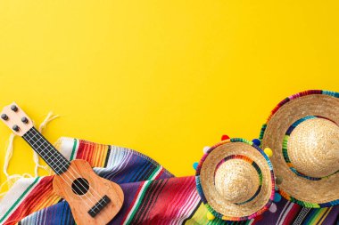Cinco de Mayo çeşitleri. Parti malzemelerinin üst görüntüsü: küçük şapkalar, el yapımı bir vihuela, renkli bir serape, canlı sarı bir ayara yerleştirilmiş.