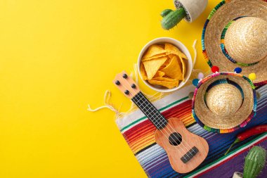 Cinco de Mayo sahnesi. Üst görünüm şenlik süsleri: küçük sombrerolar, süslü bir vihuela, saksı kaktüsü, parlak bir serape, ve altın sarısı bir yüzeye serili nachos.