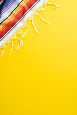 Cinco de Mayo toplama konsepti. Hardal sarısı bir yüzey üzerindeki şenlikli serape kumaşının dikey üst görünümü, kullanılabilir metin alanı