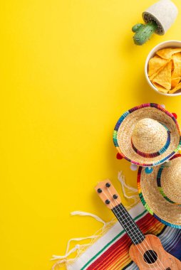 Cinco de Mayo festival düzenlemesi. İkonik öğelere dikey bir bakış: dekoratif sombrerolar, müzikal vihuela, kaktüs bitkisi, serape battaniyesi, sarı bir alana yerleştirilmiş, notlar için boşluk