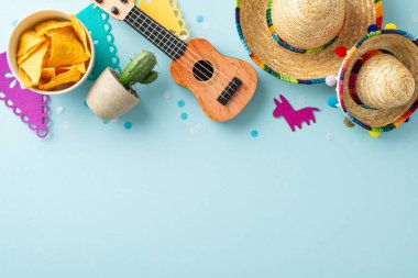 Sombreros, vihuela, kaktüs, konfeti ve yumuşak mavi arka planda bir nacho kasesi içeren Cinco de Mayo düzenlemesi.