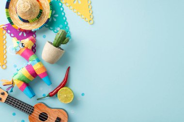 Cinco de Mayo dekorasyonlarının üst görüntüsü: şapka, bir vihuela, tencerede kaktüs, renkli bir pinata, bayrak çelengi, kırmızı biber, konfeti, pastel mavisi bir sahneye yerleştirilmiş, metin için yer